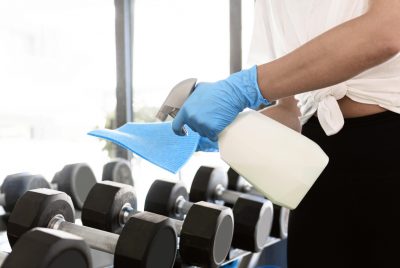 woman-with-gloves-cleaning-solution-disinfecting-gym-equipment